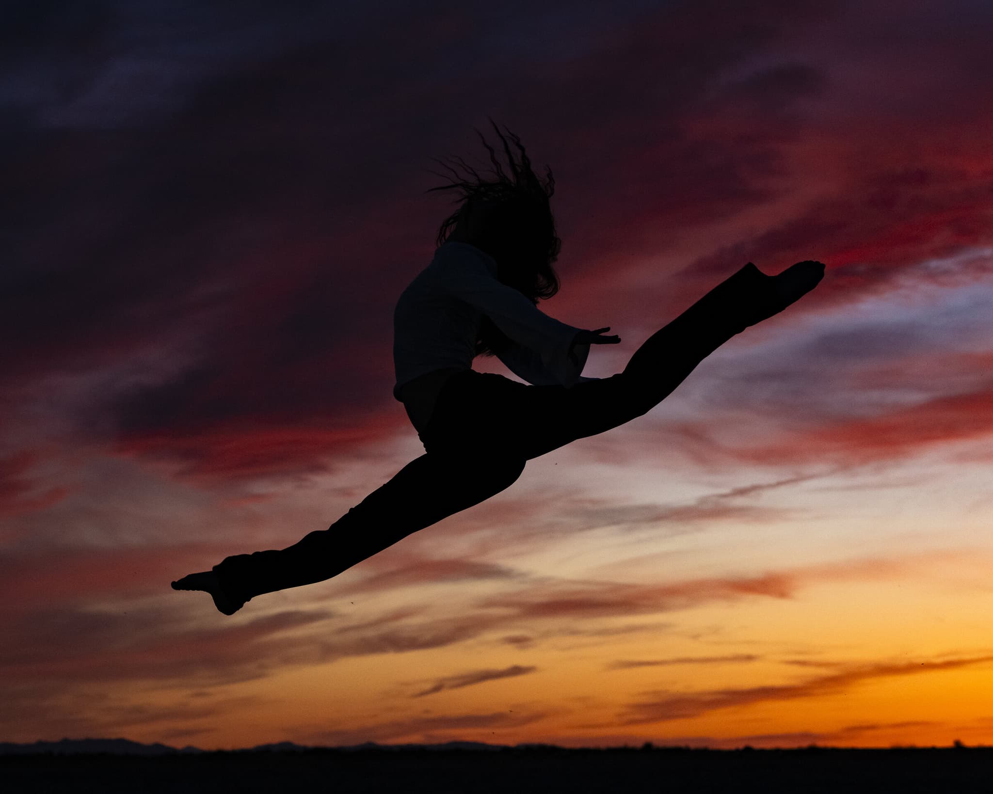 Maya Merrill performing a dramatic leap against a sunset sky
